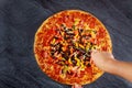 Hand cut the supreme pizza with tomato, salami, olives on black table Royalty Free Stock Photo