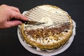 Hand cuts a cake with a knife. Tasty cake with condensed milk and poppy seeds on a black table. Royalty Free Stock Photo