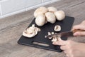 Hand cuts mushrooms with a knife on a black cutting board. Food. To cook the champignon. Vegan, vegetarian. Close-up Royalty Free Stock Photo