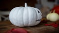 Hand decorated white pumpkin with painted face and autumn leaves on wooden table. Halloween decoration. Royalty Free Stock Photo