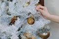 Hand decorating Christmas ornamental with silver pine cone and shiny golden decorative on white Christmas tree, Merry Christmas