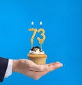 Hand delivering birthday cupcake - Candle number 73 on blue background