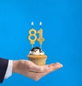Hand holding a cupcake with the number 81 candle - Birthday on blue background