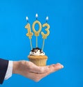 Hand delivering birthday cupcake - Candle number 103 on blue background