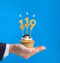 Hand delivering birthday cupcake - Candle number 119 on blue background Royalty Free Stock Photo