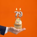 The hand that delivers cupcake with the number 79 candle - Birthday on orange background