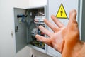 A hand in a dielectric glove reaches for the electrical panel