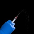 hand in a disposable glove with a syringe with red liquid on a black background.Coronavirus vaccine Royalty Free Stock Photo