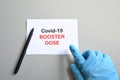 The hand of the doctor with the blue glove writes on white paper the text `Covid-19 Booster Dose`. Concept of Combating the COVI