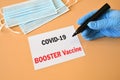 The hand of the doctor with the blue glove writes on white paper the text `Covid-19 Booster Vaccine`. Concept of Combating the