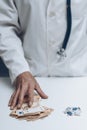 hand of doctor taking bunch of bills next to bunch of pills