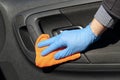 Hand of driver in blue protective glove is wiping with a cloth an interior handle of car door. Coronavirus or Covid-19 car