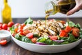 hand drizzling vinaigrette over grilled chicken salad