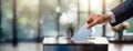 A hand dropping a ballot into a voting box, set against a blurred indoor background. Panorama with copy space. Royalty Free Stock Photo