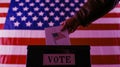A hand dropping a ballot into a voting box, with a U.S. flag in the background AI-generated Royalty Free Stock Photo