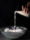 Hand dropping water over a bowl with flour on a black background Royalty Free Stock Photo