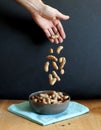 a hand drops a handful of peanuts into a bowl. black background