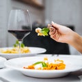 Hand eating penne pasta with mozzarella cheeze with a glass of red wine