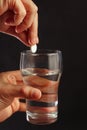 Hand with an effervescent tablet from headache over the glass of water on black background. Royalty Free Stock Photo