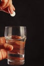 Hand with an effervescent tablet over the glass of water on black background. Royalty Free Stock Photo