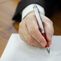 Hand of an elderly man sitting at a desk with pen and writing on a piece of paper. Concept of leaving a signature, attesting a Royalty Free Stock Photo