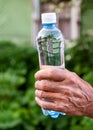 Hand of an elderly person holding a plastic bottle of fresh water, outdoors