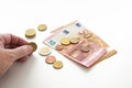 Hand of an elderly woman is counting her money, a few euro coins and banknotes, white background