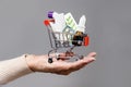 Hand of elderly woman rolls a full of medicines little shopping cart. Gray background. Concept of online shopping and