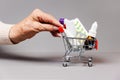 Hand of elderly woman rolls a full of medicines little shopping cart. Gray background. Concept of online shopping