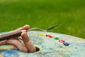 The hand of a European artist holds a mastekhin smeared in oil paint and a palette against the background of a green lawn. Blurred Royalty Free Stock Photo