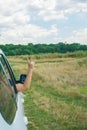 A hand extending from a white car window making a peace sign, with a field and trees in the background under a cloudy Royalty Free Stock Photo