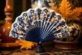 a hand fan decorated with traditional asian motifs, an electric fan in the soft focus background