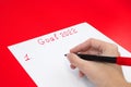 A hand with a felt-tip pen writing a list of New Year`s goals for 2022 on a sheet on a red background. The concept of planning Royalty Free Stock Photo