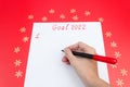 A hand with a felt-tip pen writing a list of New Year`s goals for 2022 on a sheet on a red background. The concept of planning Royalty Free Stock Photo