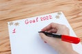 A hand with a felt-tip pen writing a list of New Year`s goals for 2022 on a sheet on a wood background. The concept of planning Royalty Free Stock Photo