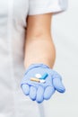 Hand of female doctor in blue glove with pile of pills of differ