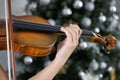Hand of a female violinist on the fingerboard of a violin with Christmas tree