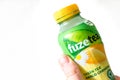 Hand and fingers holding a bottle of Fuze Tea Green Mango Chamomile drink on white background. Isolated.