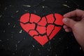 Hand fixing a broken and torn red heart paper cutout in black background. Royalty Free Stock Photo