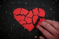 Hand fixing and repairing a broken red heart paper cutout in black background. Royalty Free Stock Photo