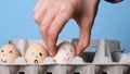 Hand folds eggs with smileys in an egg tray on blue background. Easter concept. Cultural symbol of Easter. Farm eggs