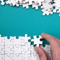 The hand folds a white jigsaw puzzle and a pile of uncombed puzzle pieces lies against the background of the blue surface. Texture Royalty Free Stock Photo