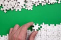 The hand folds a white jigsaw puzzle and a pile of uncombed puzzle pieces lies against the background of the green surface. Textur Royalty Free Stock Photo