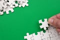 The hand folds a white jigsaw puzzle and a pile of uncombed puzzle pieces lies against the background of the green surface. Textur Royalty Free Stock Photo