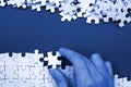 The hand folds a white jigsaw puzzle and a pile of uncombed puzzle pieces lies against the background of phantom classic blue Royalty Free Stock Photo