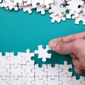 The hand folds a white jigsaw puzzle and a pile of uncombed puzzle pieces lies against the background of the blue surface. Texture Royalty Free Stock Photo