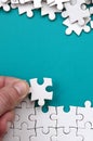 The hand folds a white jigsaw puzzle and a pile of uncombed puzzle pieces lies against the background of the blue surface. Texture Royalty Free Stock Photo