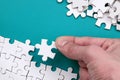 The hand folds a white jigsaw puzzle and a pile of uncombed puzzle pieces lies against the background of the blue surface. Texture Royalty Free Stock Photo