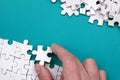 The hand folds a white jigsaw puzzle and a pile of uncombed puzzle pieces lies against the background of the blue surface. Texture Royalty Free Stock Photo