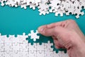 The hand folds a white jigsaw puzzle and a pile of uncombed puzzle pieces lies against the background of the blue surface. Texture Royalty Free Stock Photo